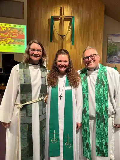 Three clergy members smiling in green and white robes inside a church.
