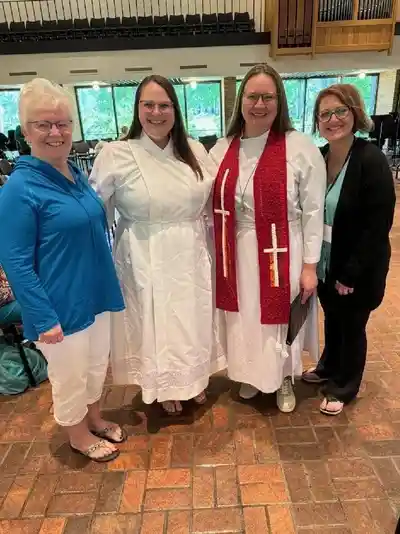 Four women standing together, two dressed in white religious robes.