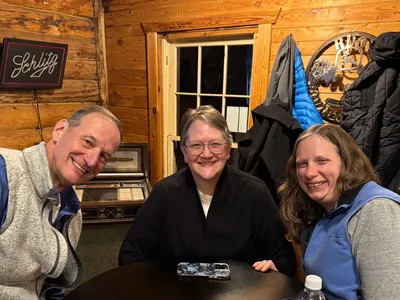 Three people smiling inside a cozy wooden room.