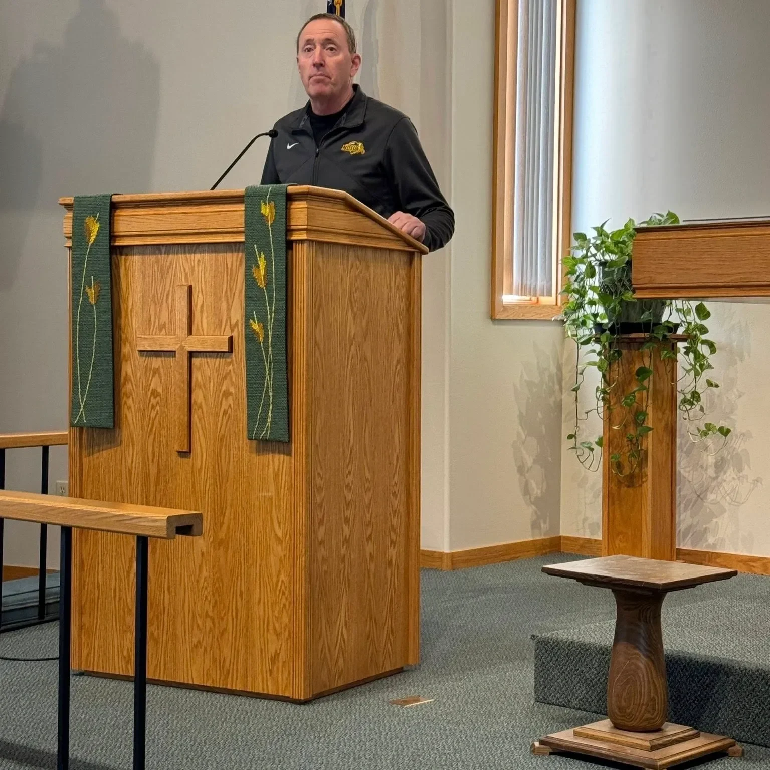 Man speaking at a church podium with a cross on it.